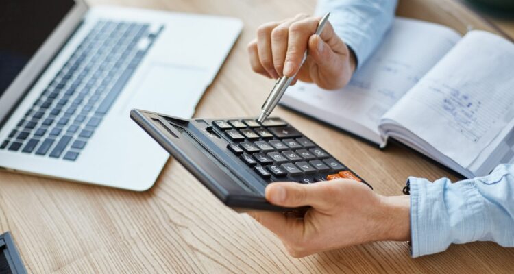 une personne calculant les paies des salariés à l'aide d'une calculatrice