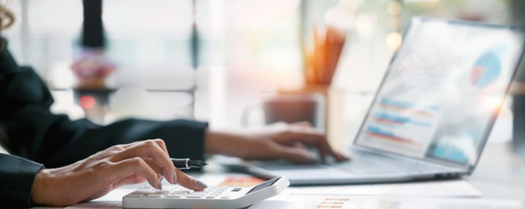 une femme calculant à la fois sur une calculatrice et sur son ordinateur