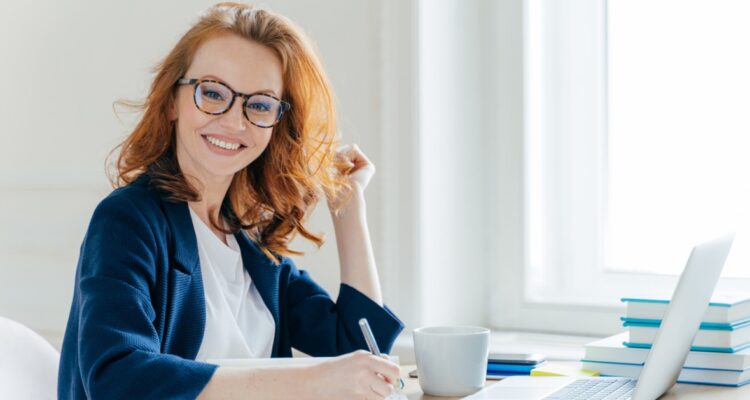 une femme rousse souriante devant son ordinateur