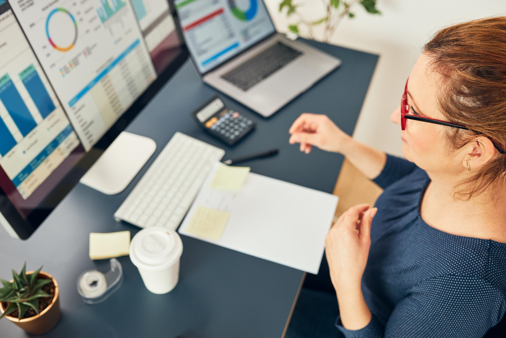 une femme au travail devant un ordinateur et plusieurs écrans